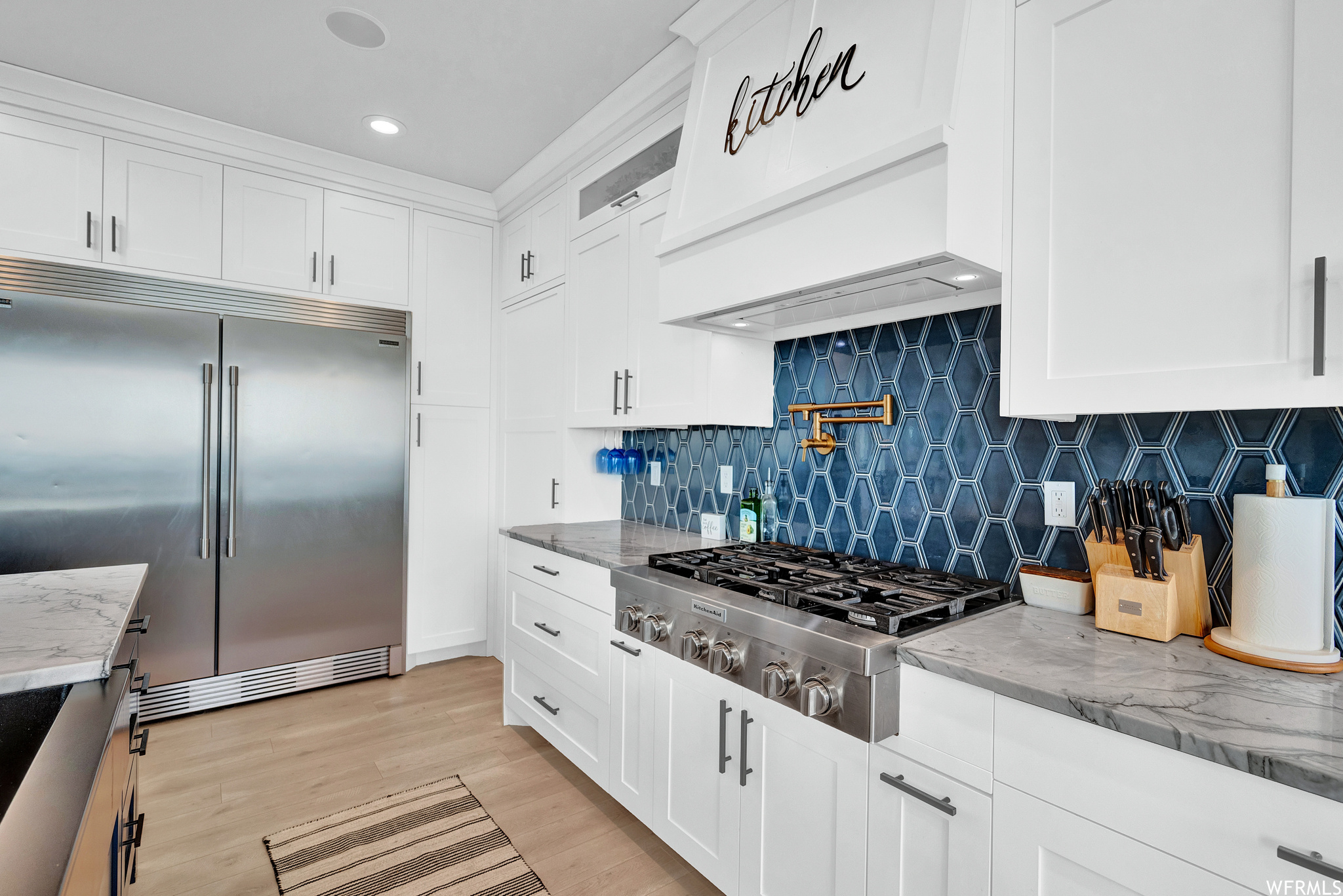 Kitchen featuring exhaust hood, refrigerator, gas cooktop, light floors, light countertops, and white cabinets