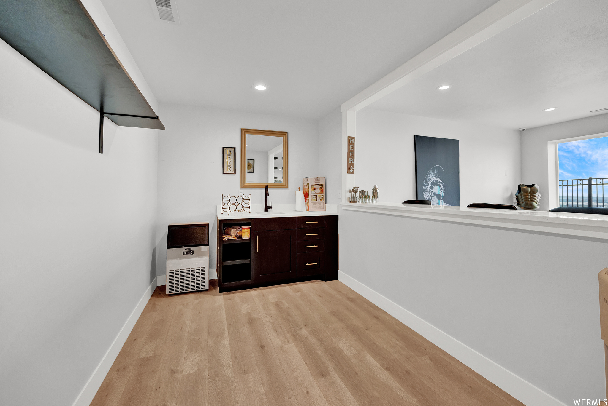 Bar featuring natural light, light hardwood flooring, dark brown cabinetry, and light countertops