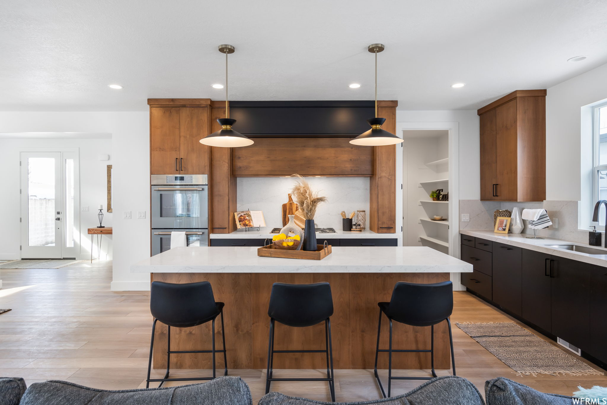 Kitchen featuring a breakfast bar, stainless steel double oven, light parquet floors, light countertops, brown cabinetry, and pendant lighting