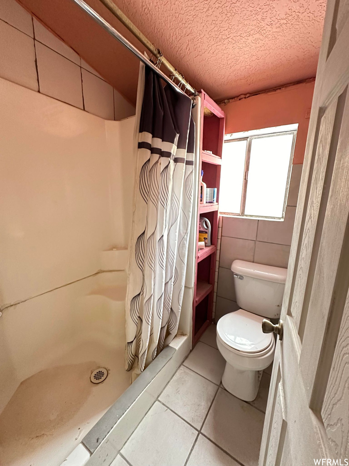 Bathroom with toilet, a shower with curtain, tile walls, a textured ceiling, and tile floors