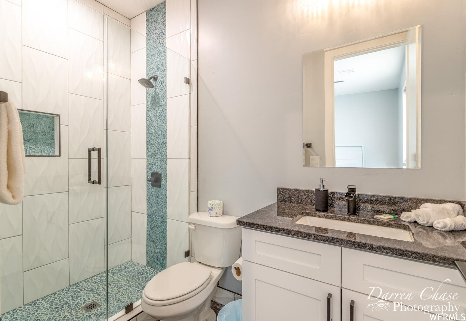 Full bathroom featuring toilet, mirror, vanity, and shower with shower door