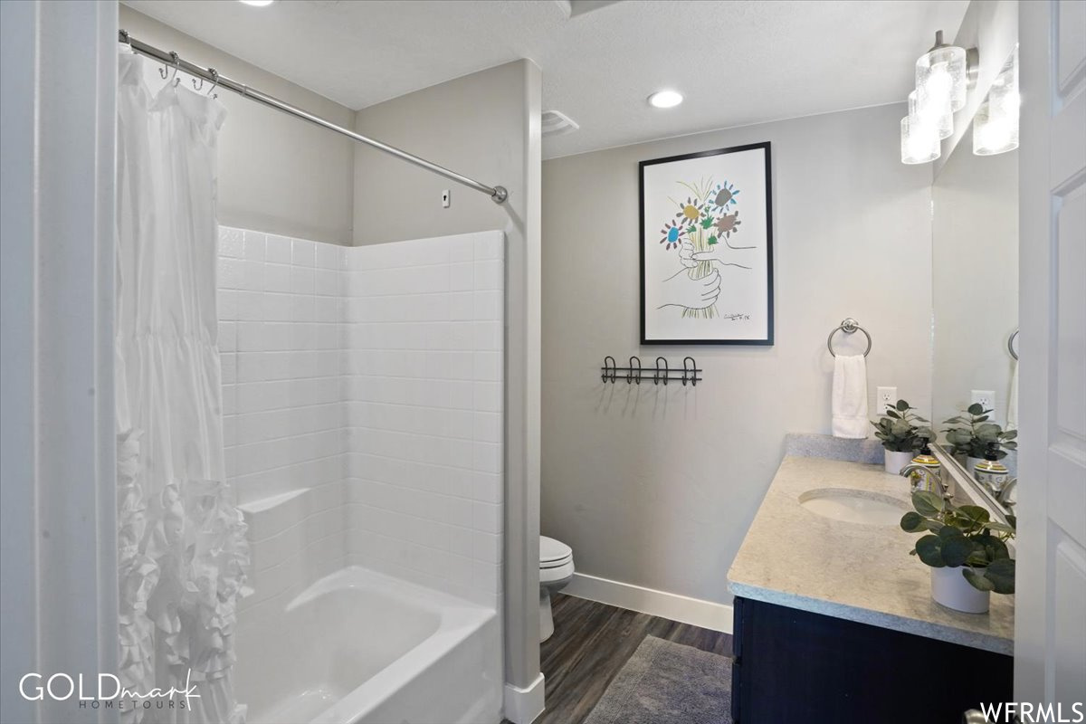 Full bathroom featuring hardwood flooring, washtub / shower combination, shower curtain, mirror, large vanity, and toilet