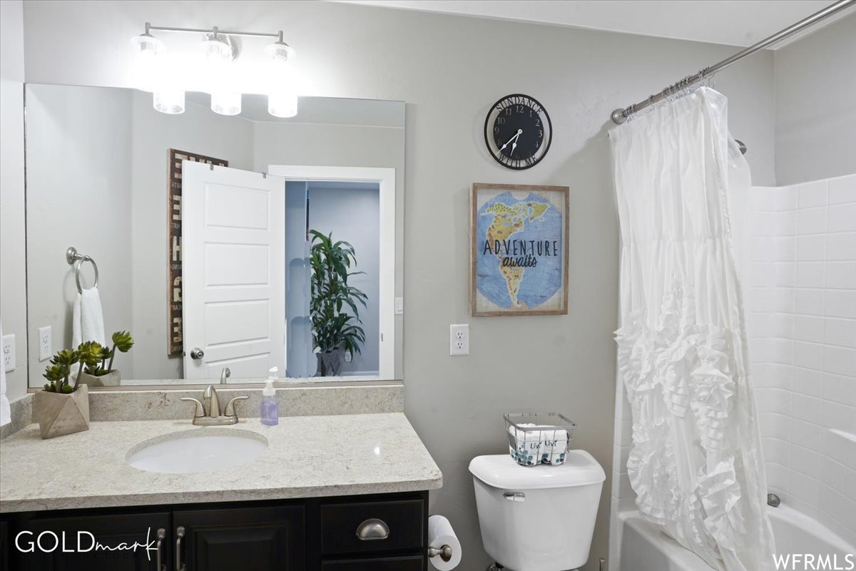 Full bathroom with shower curtain, mirror, vanity with extensive cabinet space, shower / bathtub combination, and toilet