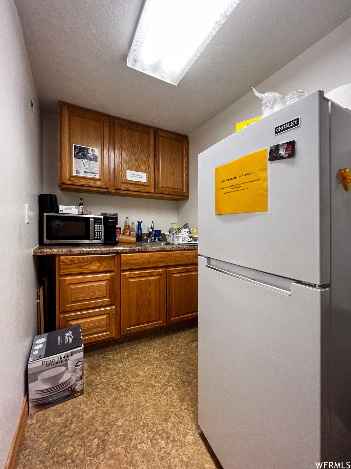 Break room with a textured ceiling, brown cabinets, white refrigerator, and tile flooring
