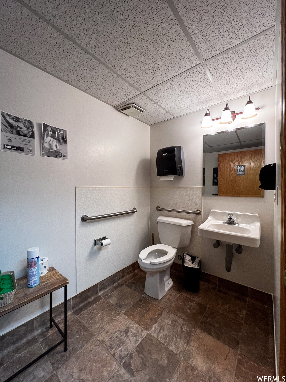 Bathroom featuring dark tile flooring, a drop ceiling, mirror, and washbasin