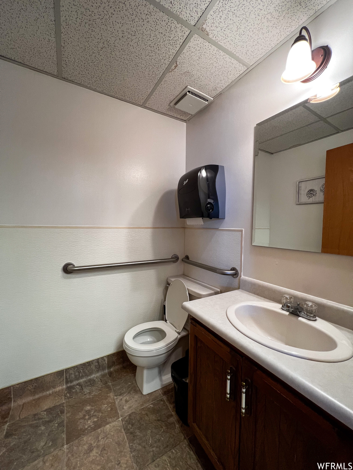 Bathroom featuring vanity, a drop ceiling, dark tile floors, and mirror