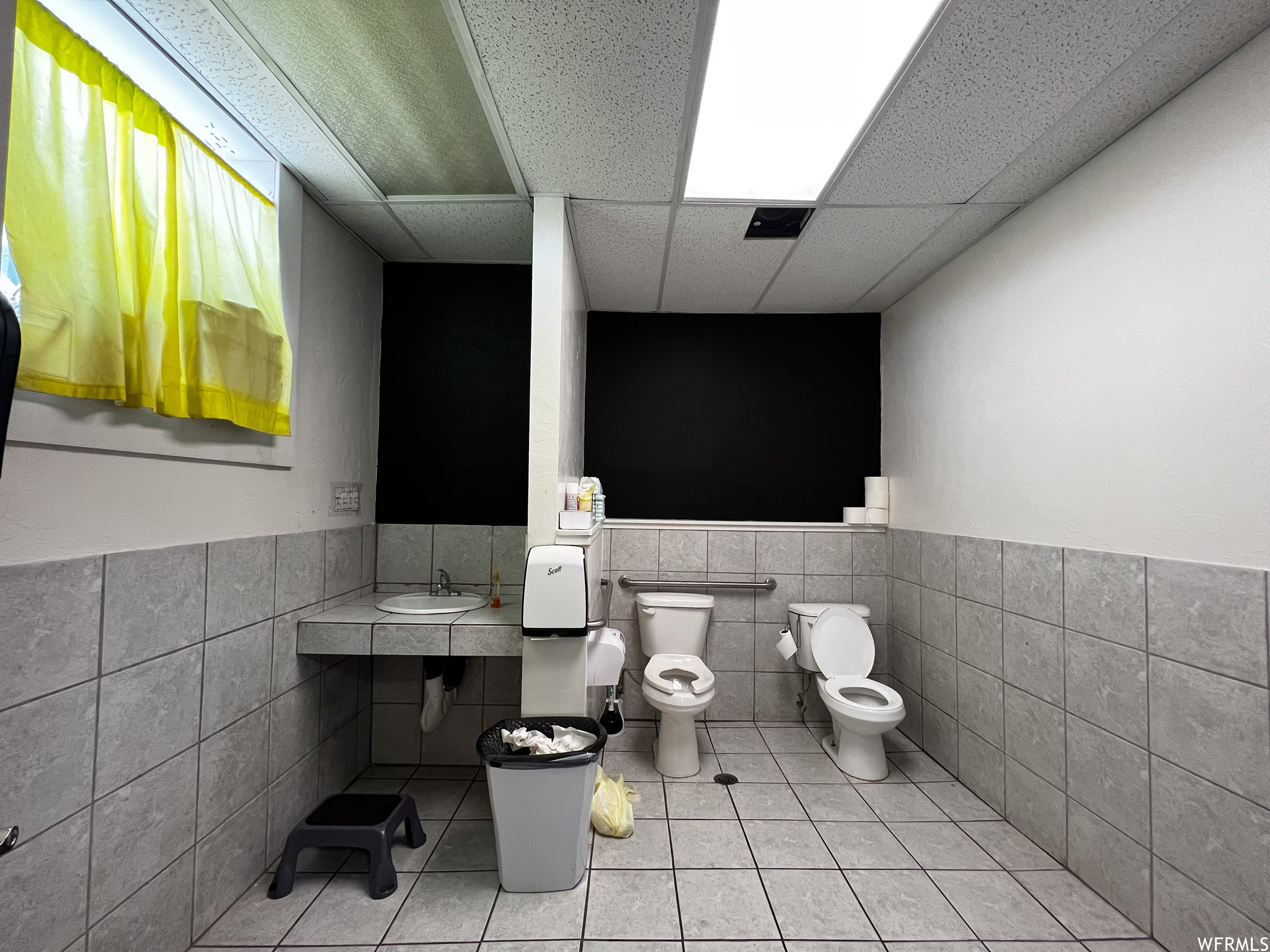 Bathroom with tile walls, light tile floors, a drop ceiling, and sink