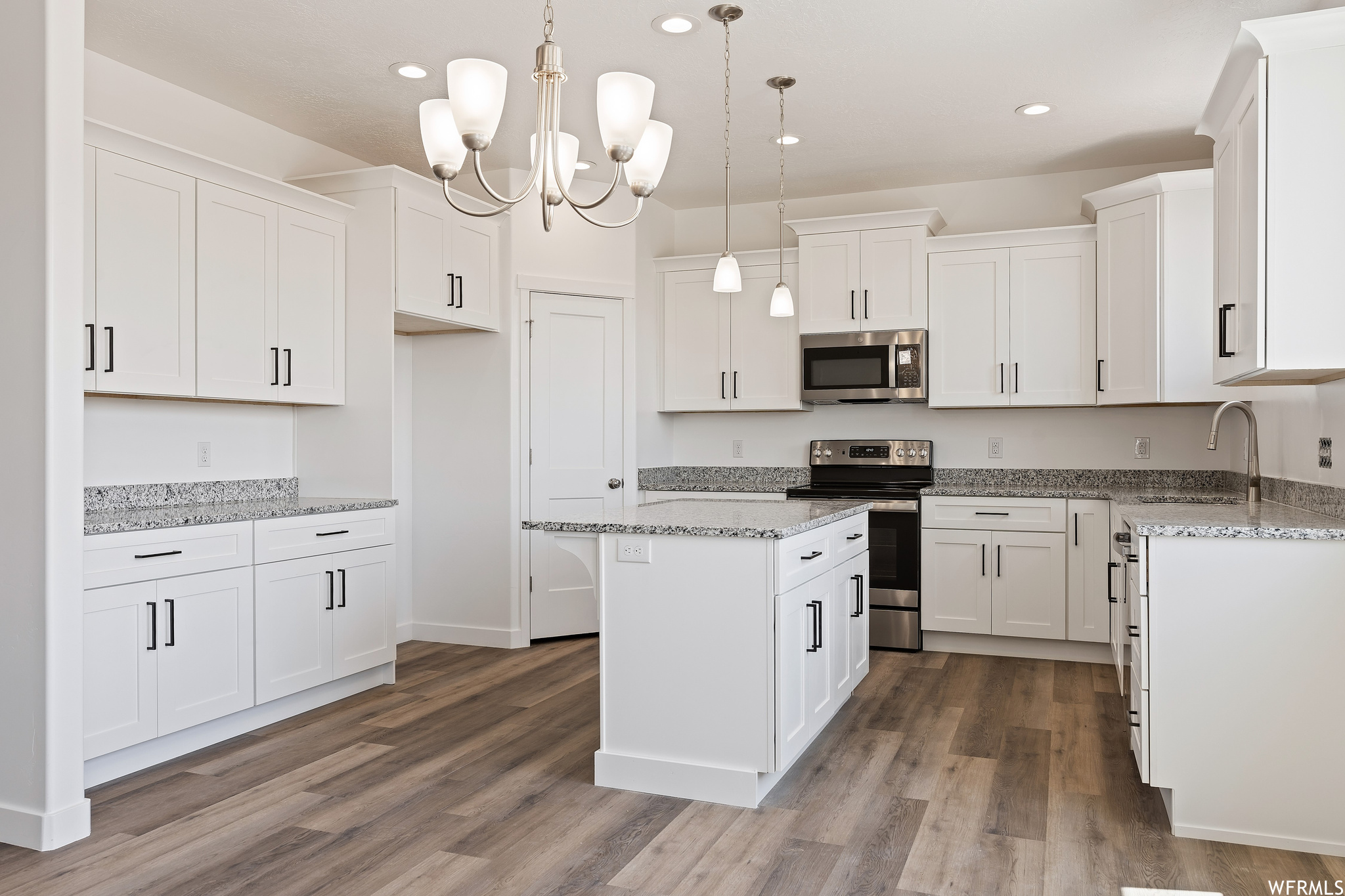 Kitchen with white cabinetry, pendant lighting, dark hardwood flooring, a chandelier, light stone countertops, and appliances with stainless steel finishes