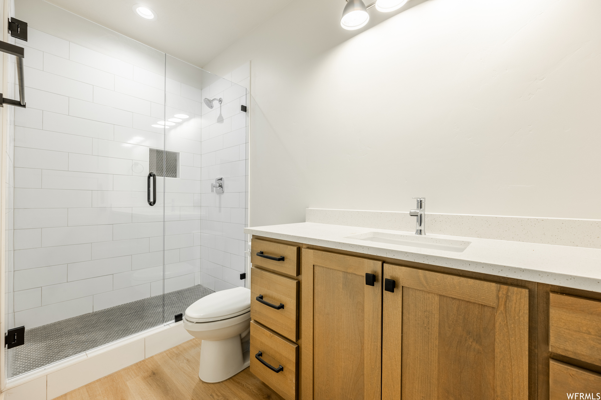 Basement Bathroom featuring vanity, light hardwood floors, and a shower with door