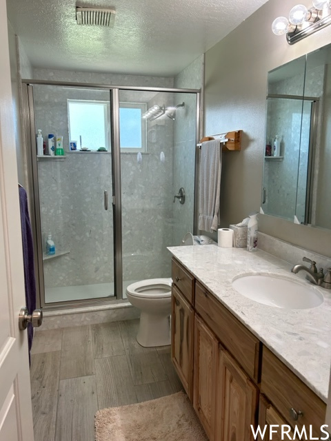 Bathroom featuring a textured ceiling, a shower with shower door, mirror, and vanity