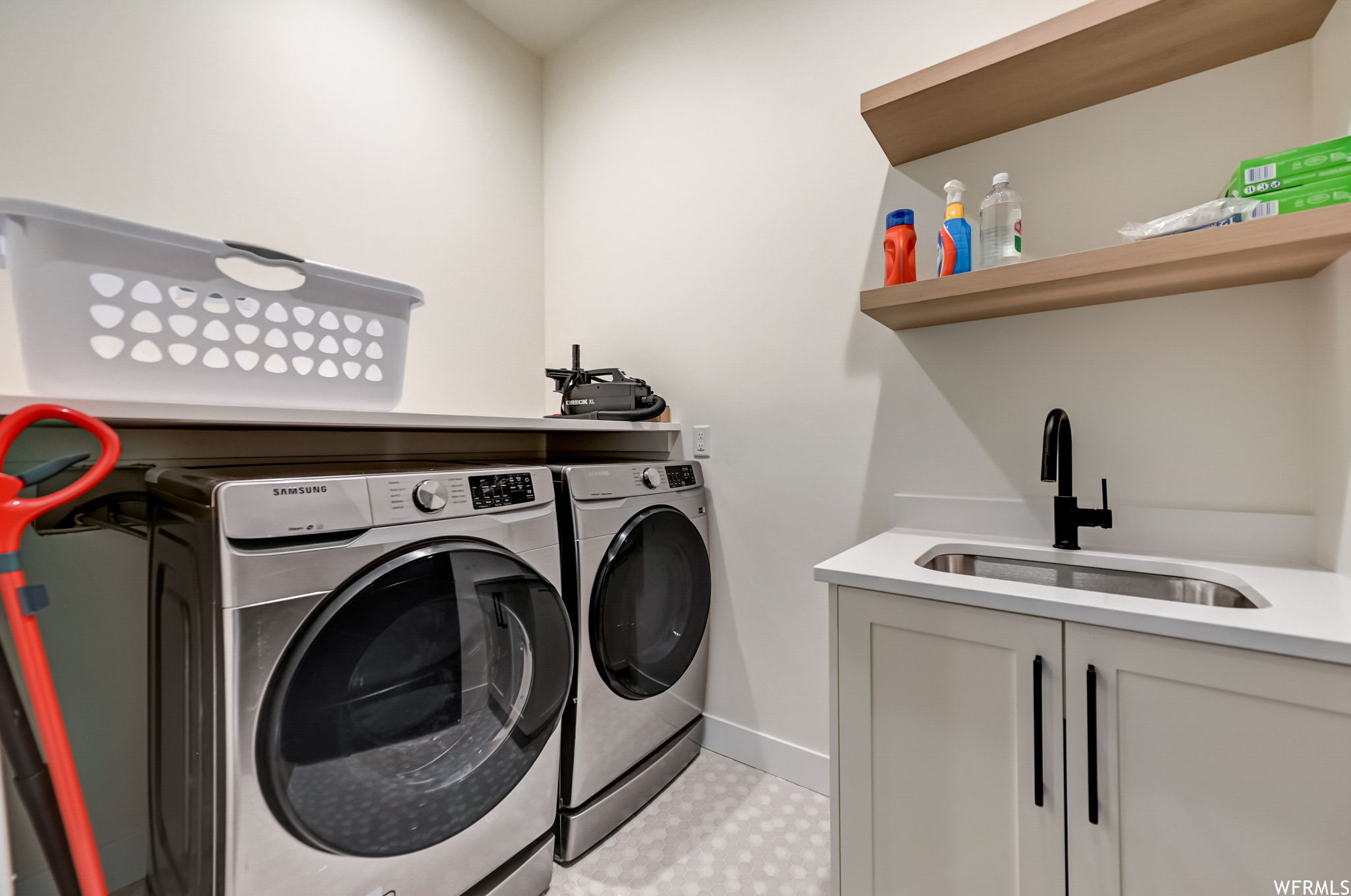 Clothes washing area featuring washer and clothes dryer, cabinets, sink, and light tile floors