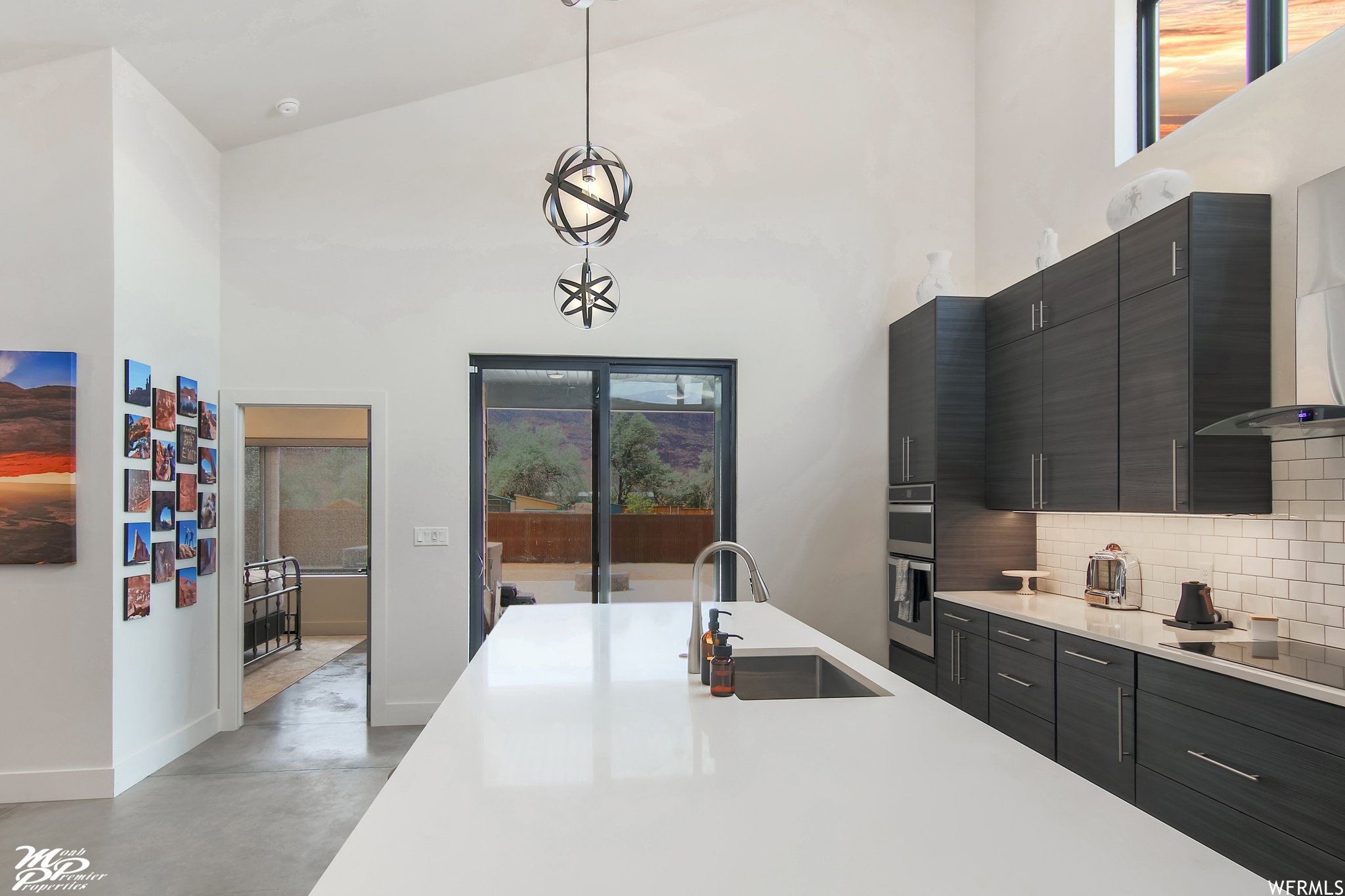 Kitchen featuring stainless steel double oven, lofted ceiling, decorative light fixtures, dark brown cabinetry, light countertops, backsplash, a high ceiling, and black electric cooktop