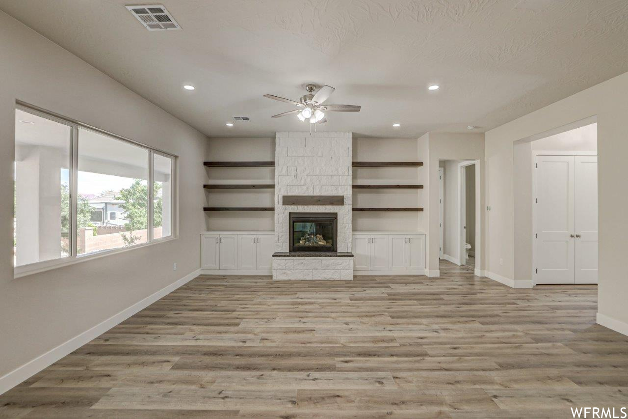 Living room featuring built in features, light hardwood flooring, a textured ceiling, a fireplace, and ceiling fan