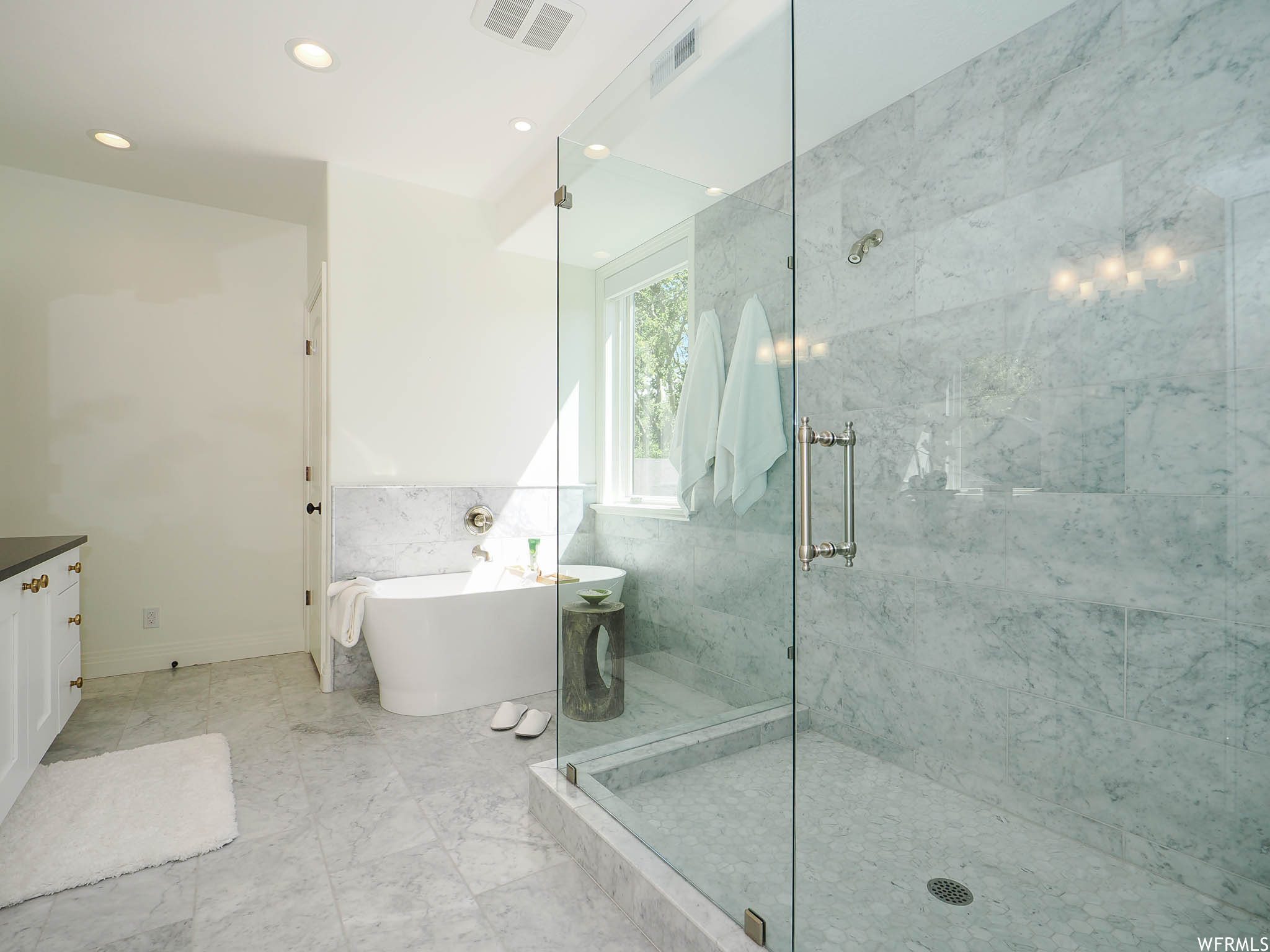 Bathroom featuring separate shower and tub, light tile floors, tile walls, and vanity