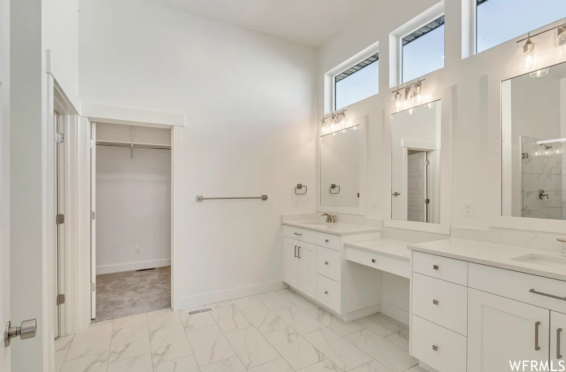 Bathroom with dual bowl vanity, mirror, light tile floors, and a shower