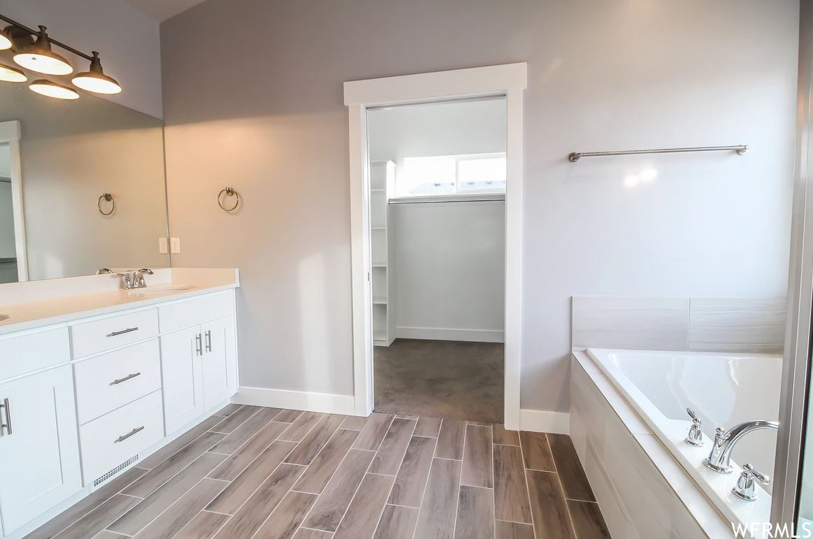 Bathroom featuring tiled tub, vanity, and mirror