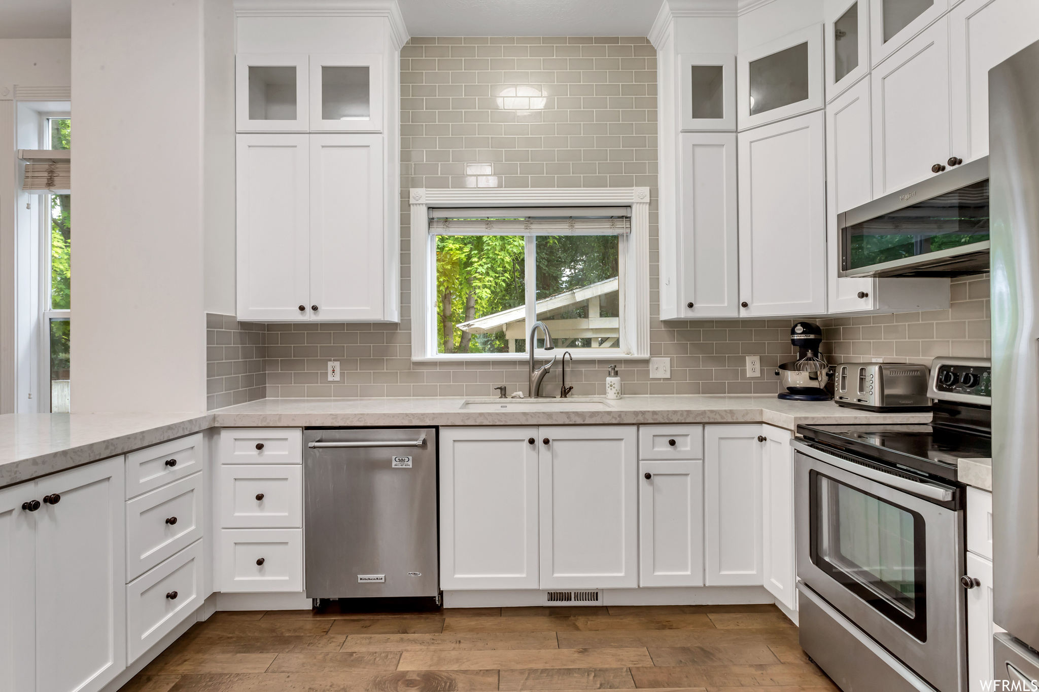 Kitchen with hardwood floors, stainless steel appliances, backsplash, white cabinets, and light countertops