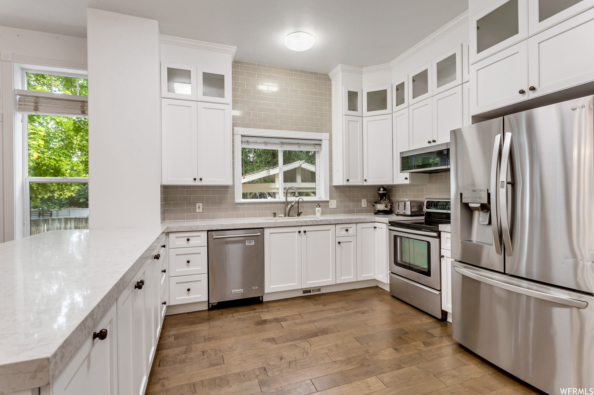 Kitchen featuring wood-type flooring, light countertops, backsplash, stainless steel appliances, and white cabinetry