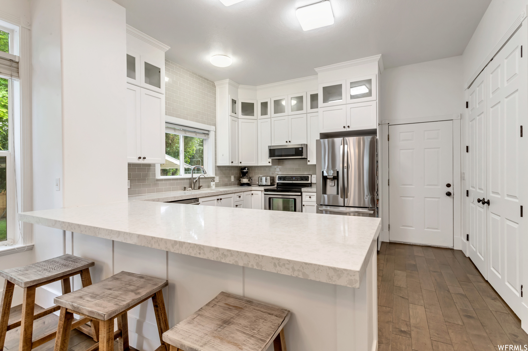 Kitchen featuring light hardwood floors, light countertops, backsplash, stainless steel appliances, and white cabinetry