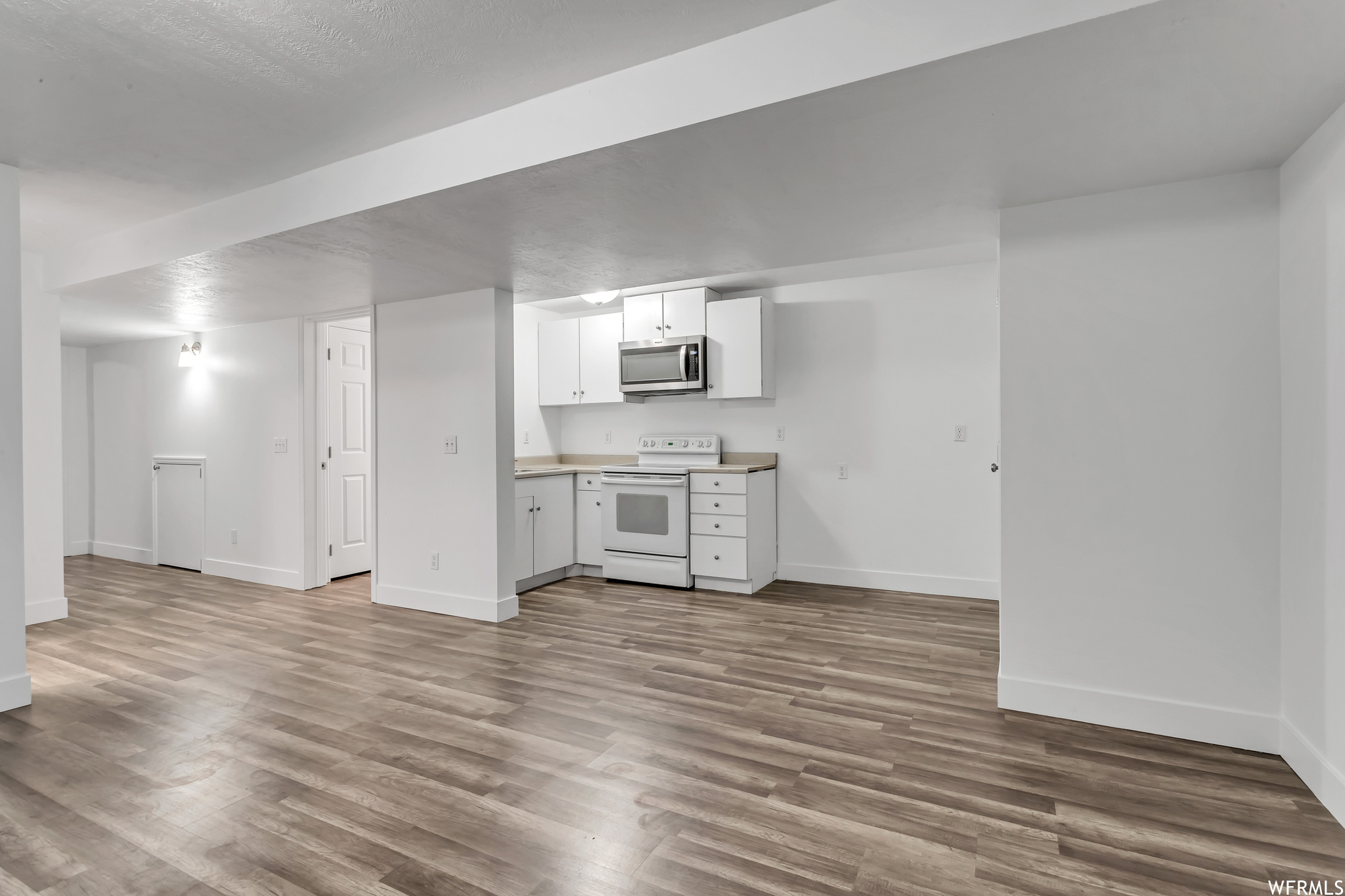Kitchen with white range, light hardwood floors, white cabinetry, and light countertops