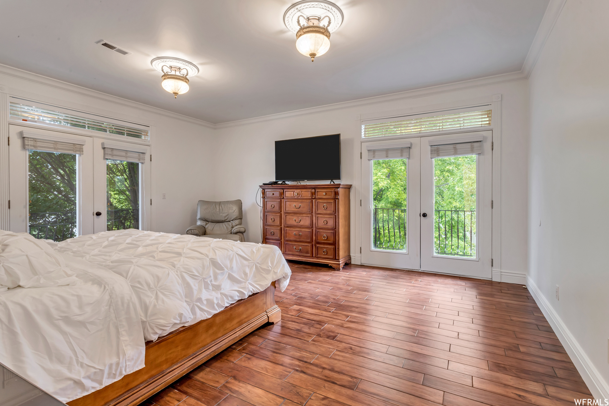 Bedroom featuring light parquet floors, crown molding, multiple windows, and french doors