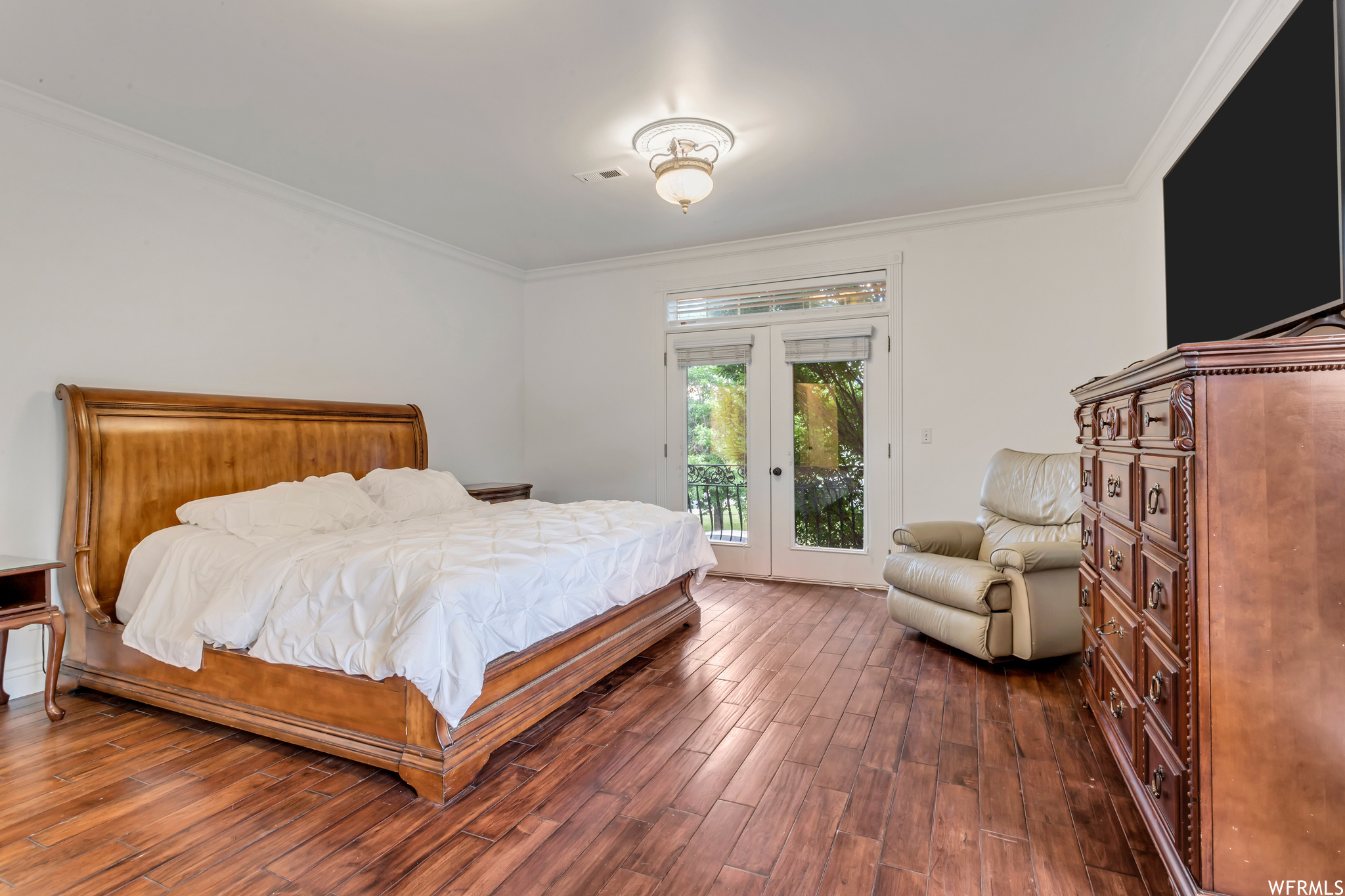 Hardwood floored bedroom with ornamental molding and french doors