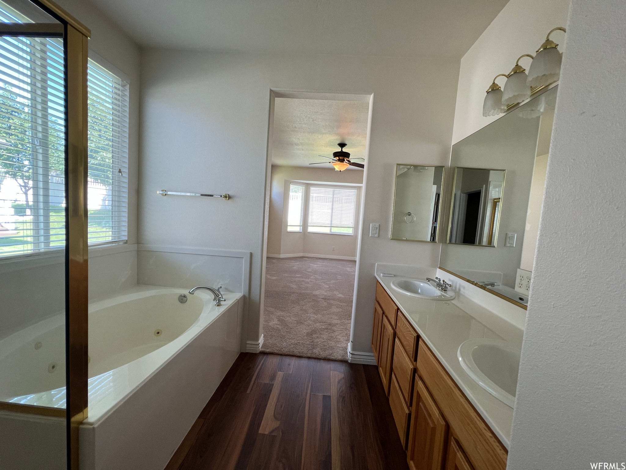 Bathroom featuring double sink vanity, a washtub, dark parquet floors, ceiling fan, and mirror