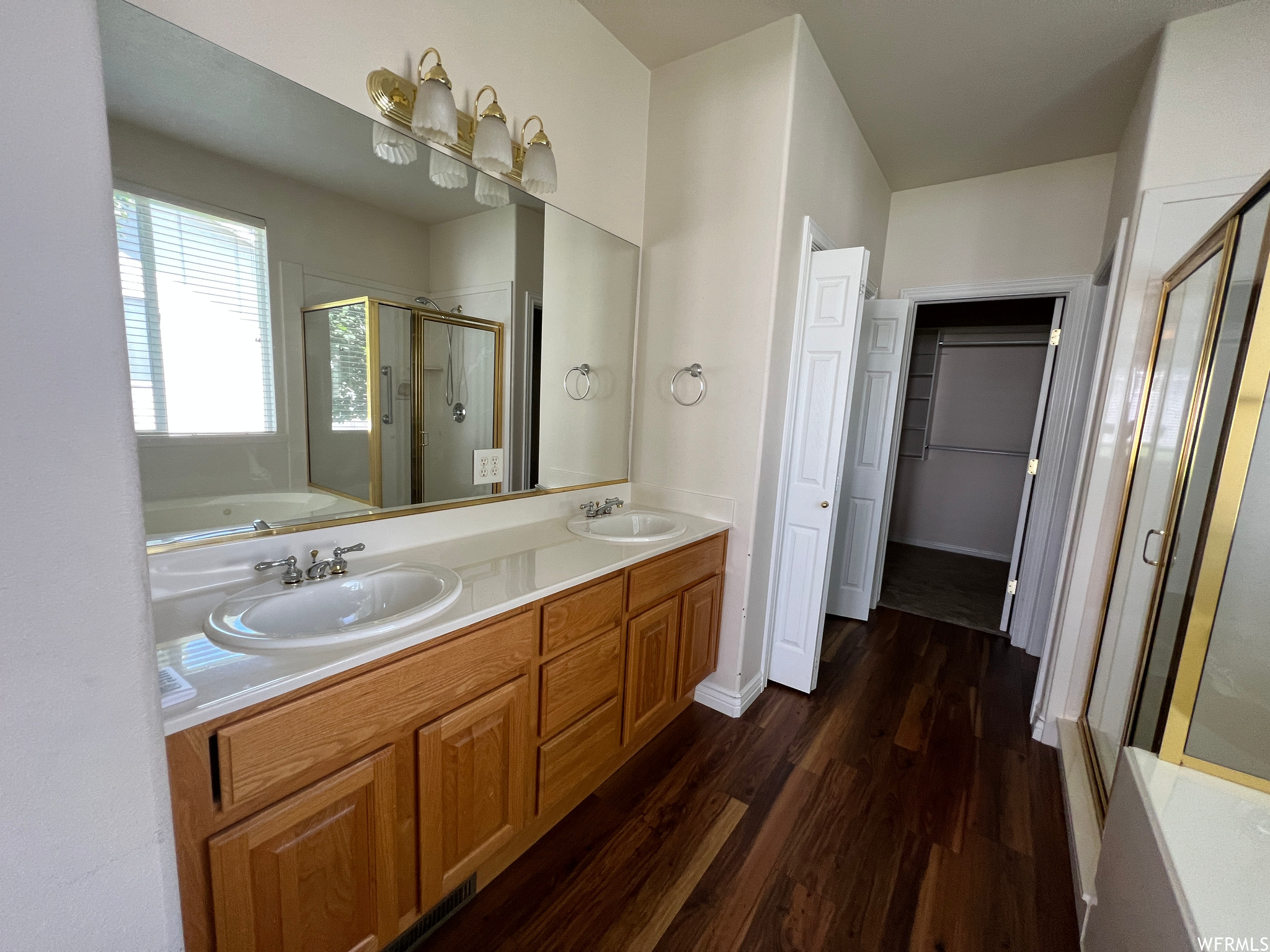 Bathroom featuring dark hardwood flooring, double large vanity, separate shower and tub enclosures, and mirror