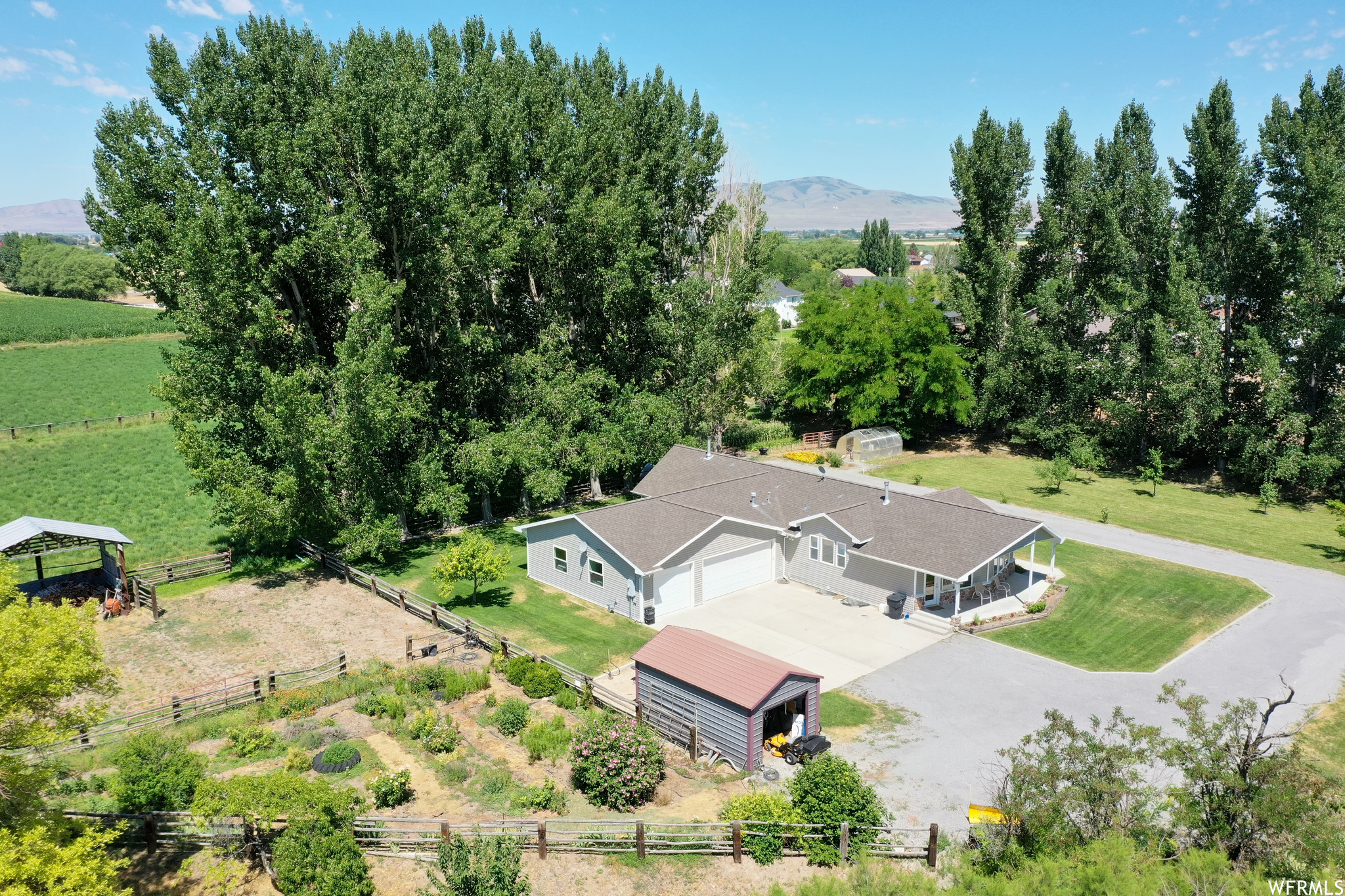 View of property featuring custom home, corrals, pasture, mature landscaping and hay field behind the house.