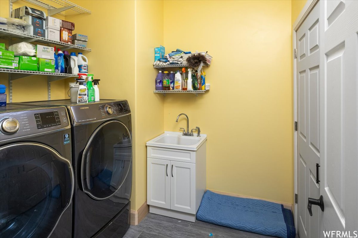 Laundry area with sink, dark hardwood / wood-style flooring, separate washer and dryer, and cabinets