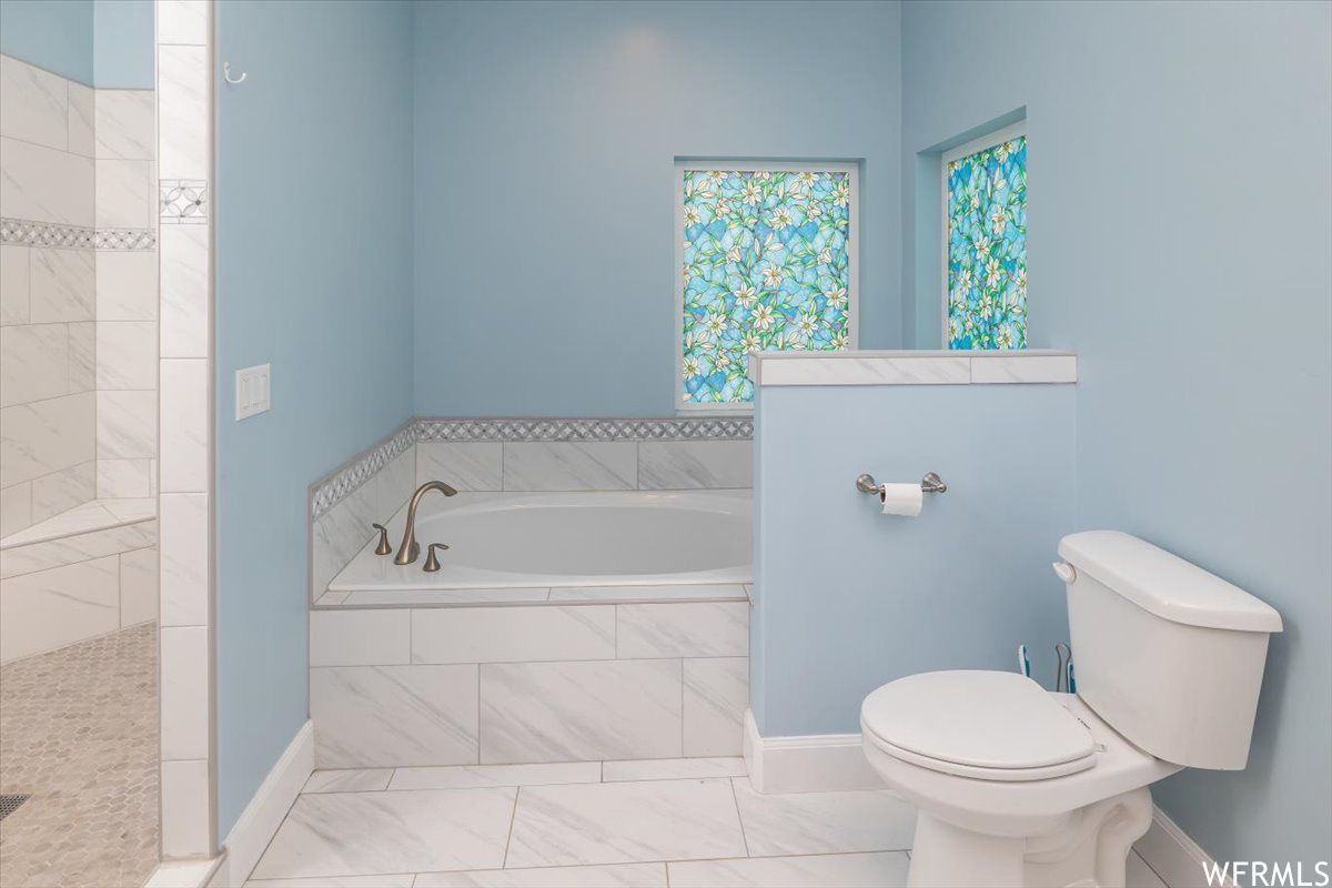 Bathroom featuring toilet, tile flooring, and a relaxing tiled bath