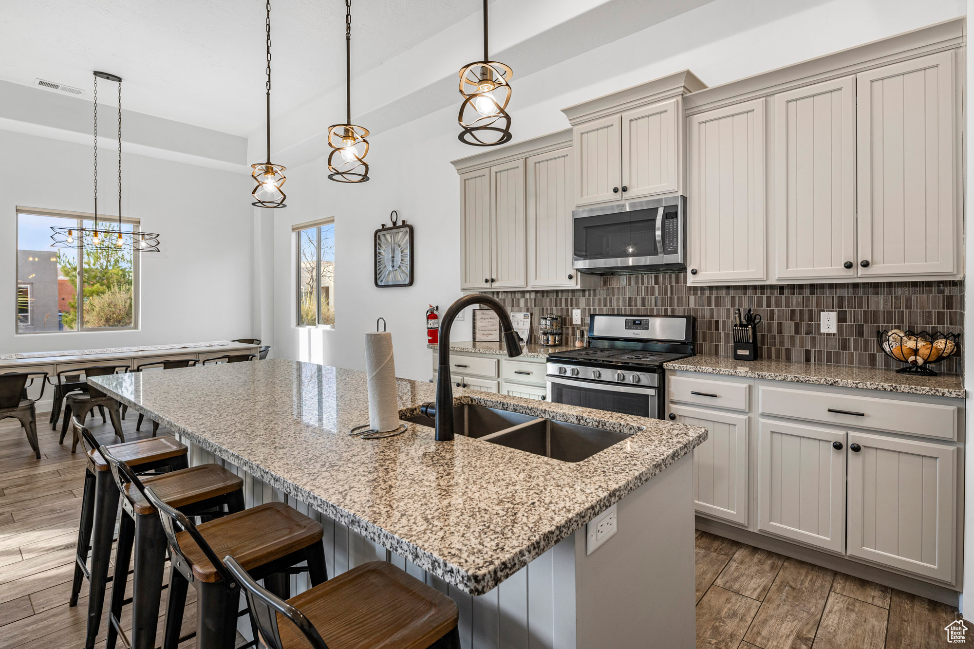 Kitchen featuring light hardwood / wood-style floors, tasteful backsplash, a notable chandelier, hanging light fixtures, and appliances with stainless steel finishes