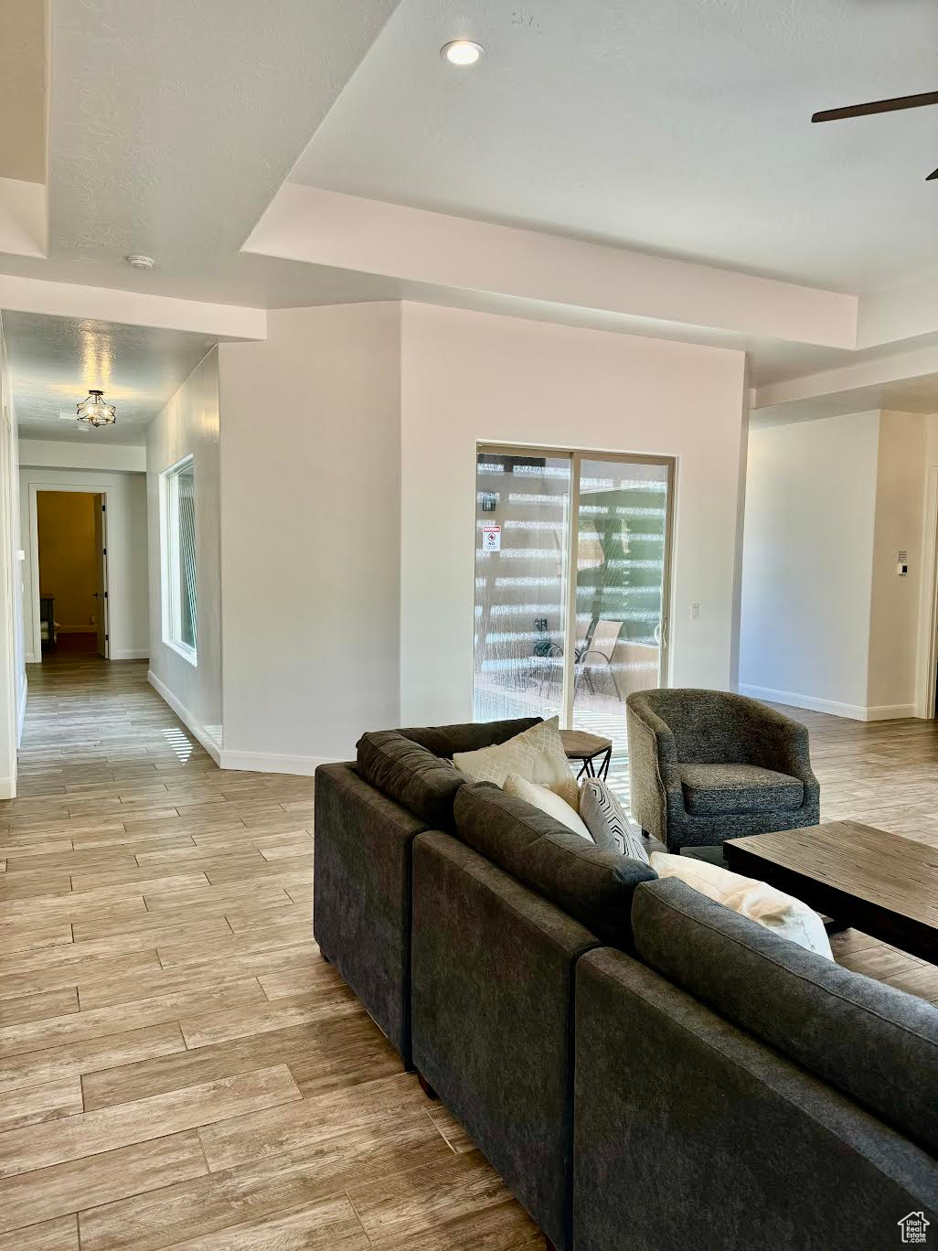 Living room featuring light wood-type flooring, ceiling fan, and a raised ceiling