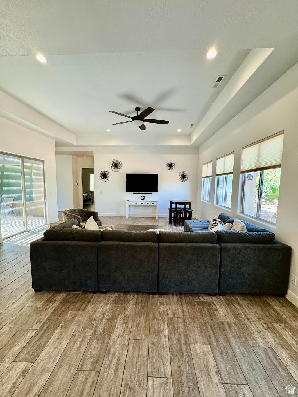 Living room with a raised ceiling, light hardwood / wood-style flooring, and ceiling fan