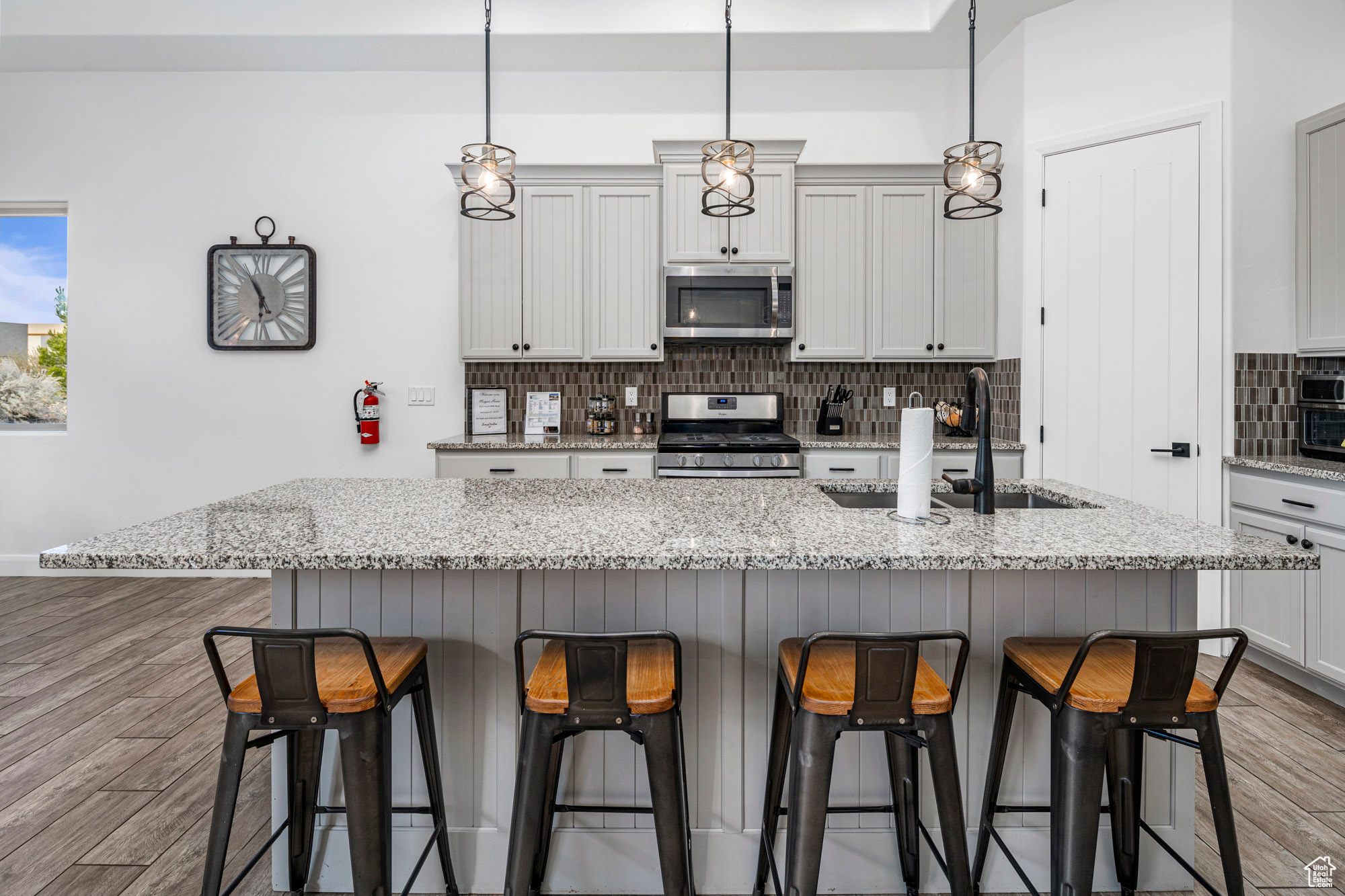 Kitchen with light hardwood / wood-style floors, pendant lighting, a breakfast bar area, light stone countertops, and appliances with stainless steel finishes