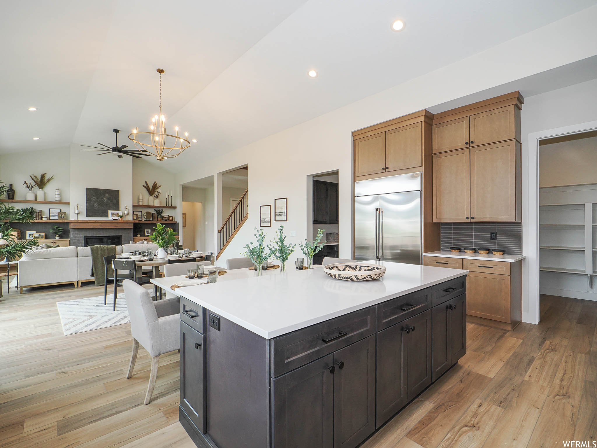 Kitchen with stainless steel built in refrigerator, a kitchen island with sink, a fireplace, lofted ceiling, light countertops, backsplash, light hardwood floors, and ceiling fan