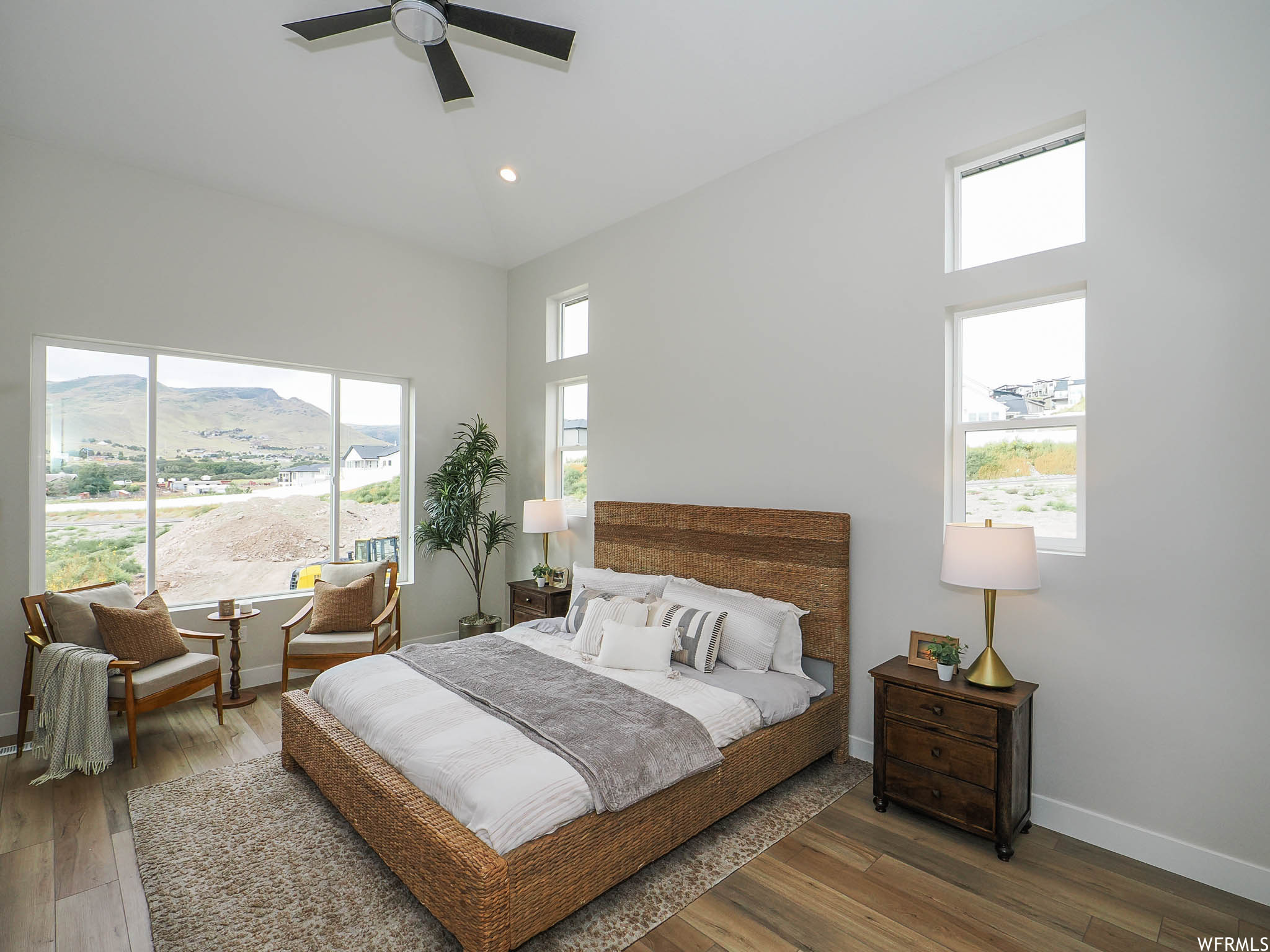 Bedroom featuring multiple windows, light hardwood flooring, a high ceiling, and ceiling fan