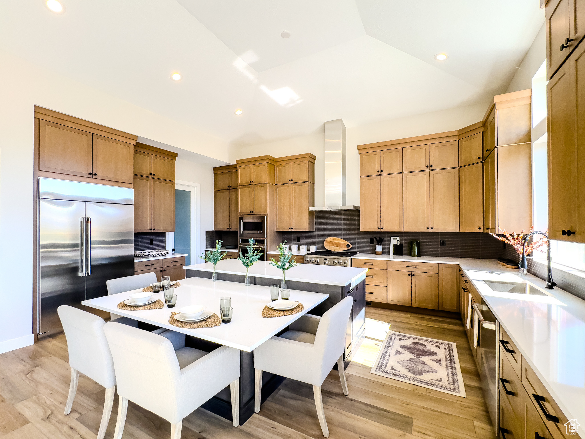 Kitchen with vaulted ceiling, a kitchen island, built in appliances, sink, and wall chimney range hood