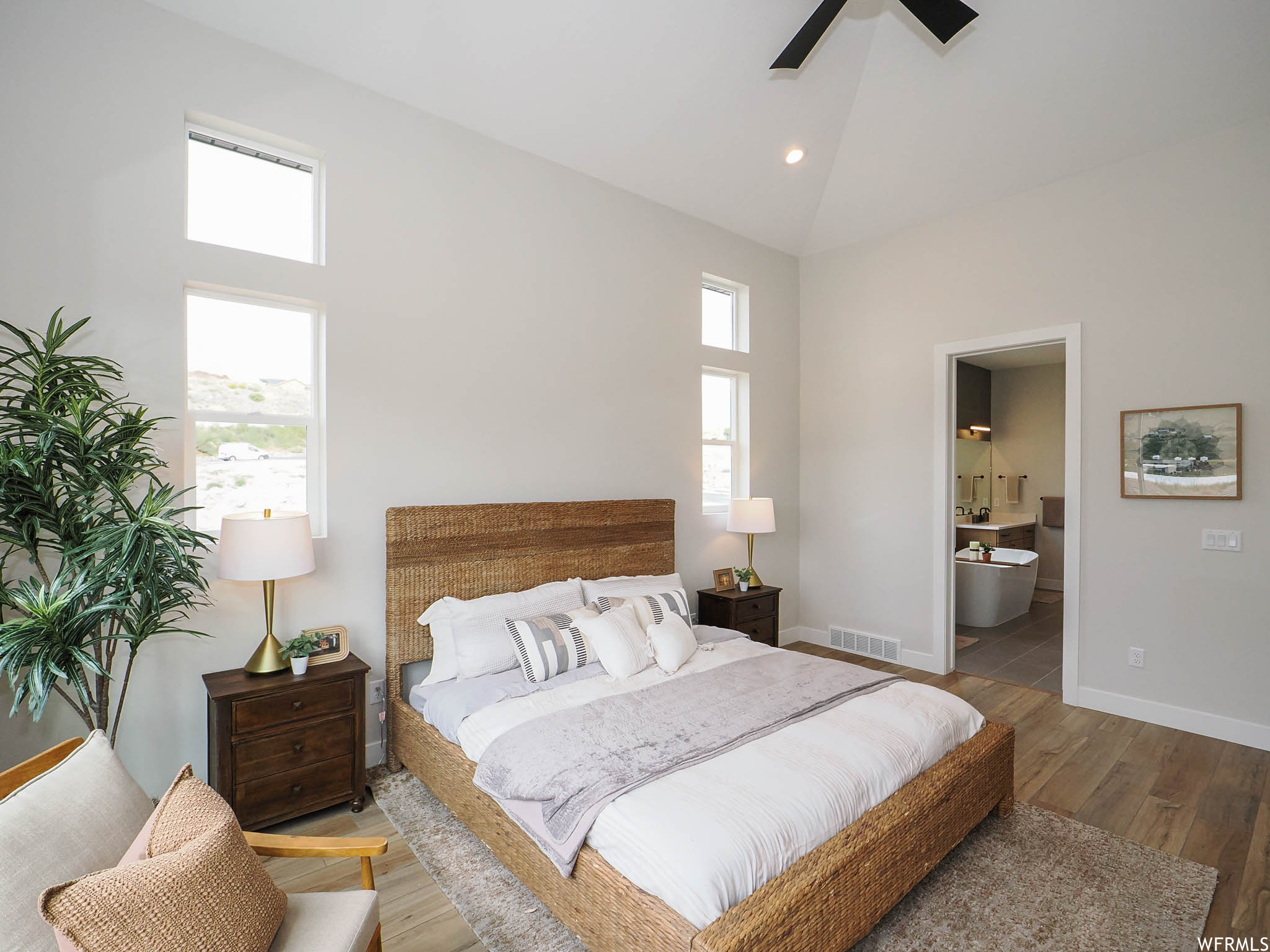 Bedroom featuring multiple windows, vaulted ceiling, a high ceiling, and light hardwood flooring