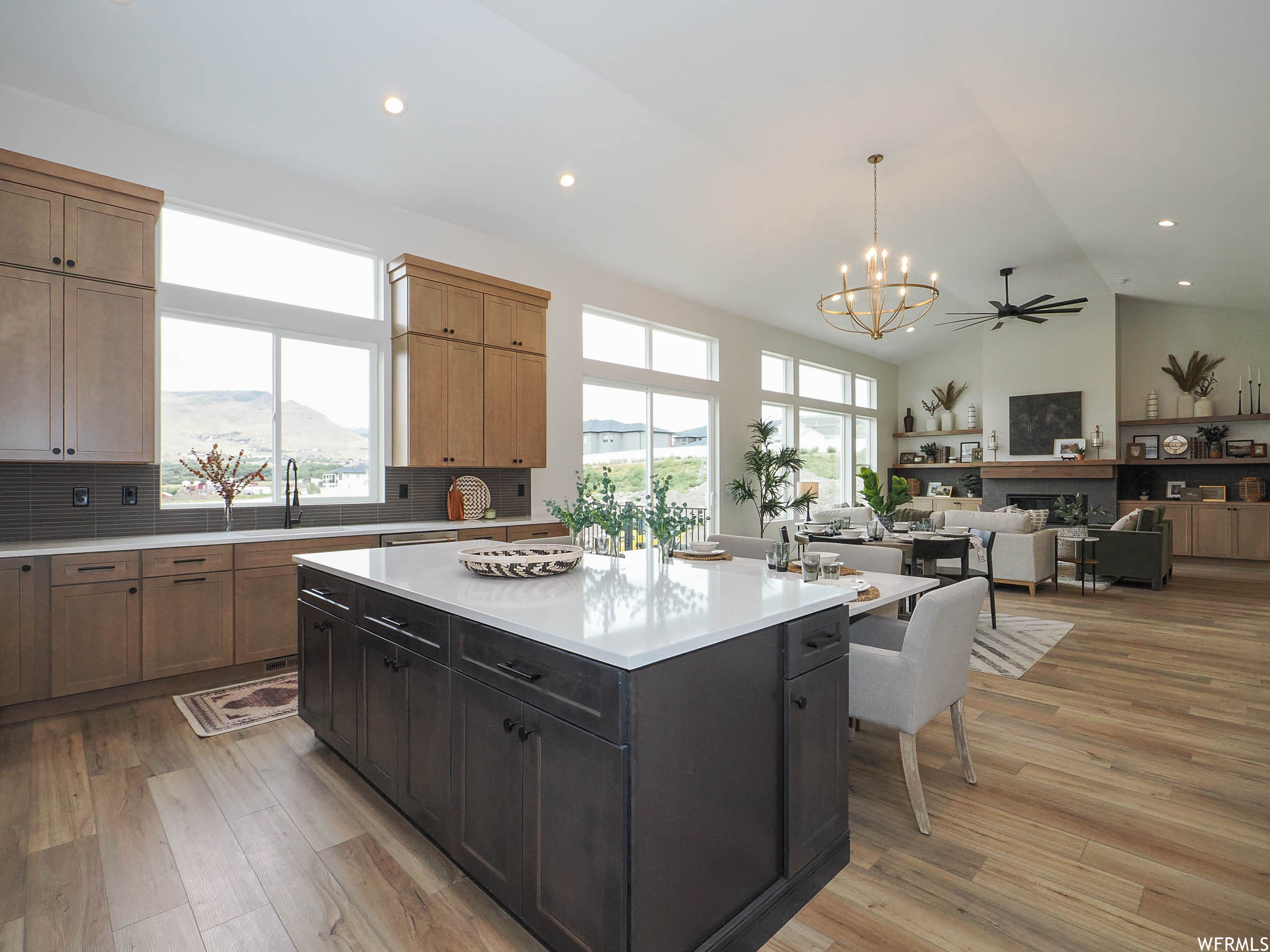 Kitchen featuring a kitchen island with sink, lofted ceiling, light countertops, ceiling fan with notable chandelier, light hardwood flooring, backsplash, and a high ceiling