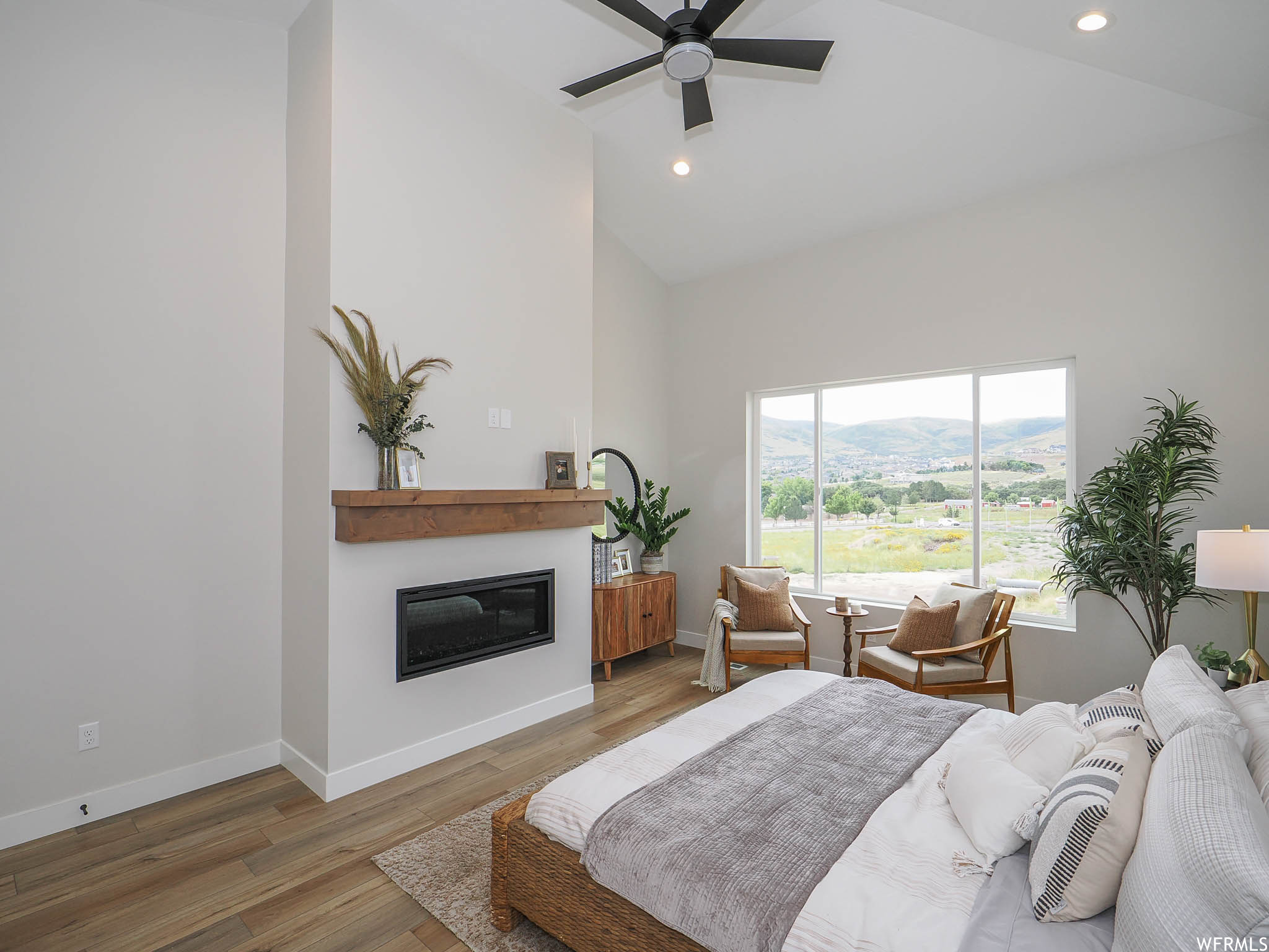 Hardwood floored bedroom featuring a fireplace, vaulted ceiling, a high ceiling, and ceiling fan