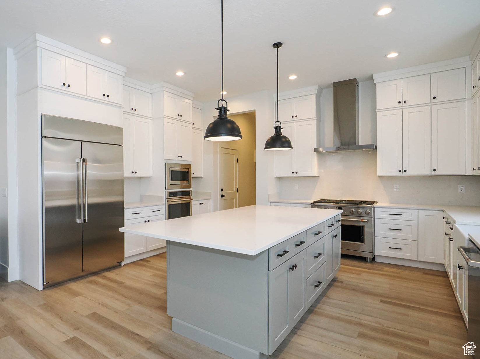 Kitchen featuring built in appliances, decorative light fixtures, wall chimney exhaust hood, a center island, and light wood-type flooring