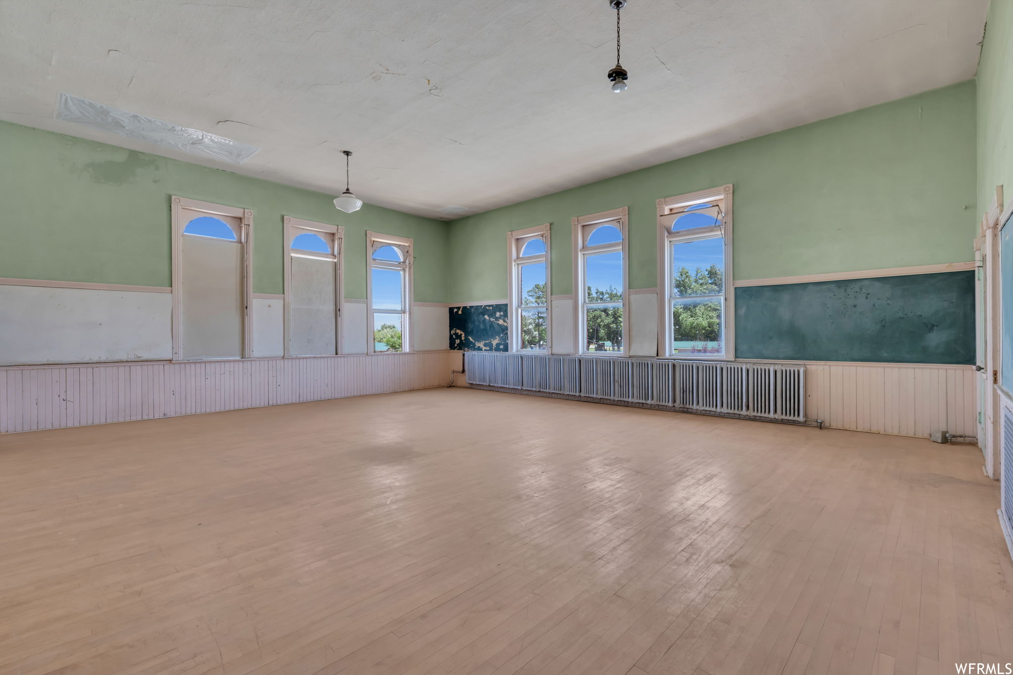 View of wood floored classroom with large windows and chalk board walls