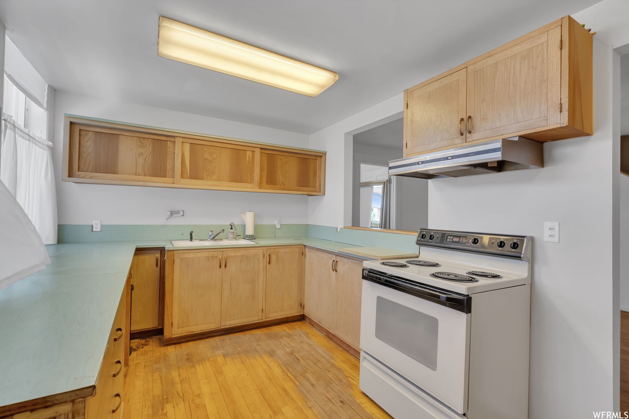 Kitchen featuring light hardwood floors, light countertops, range hood, and white electric range oven