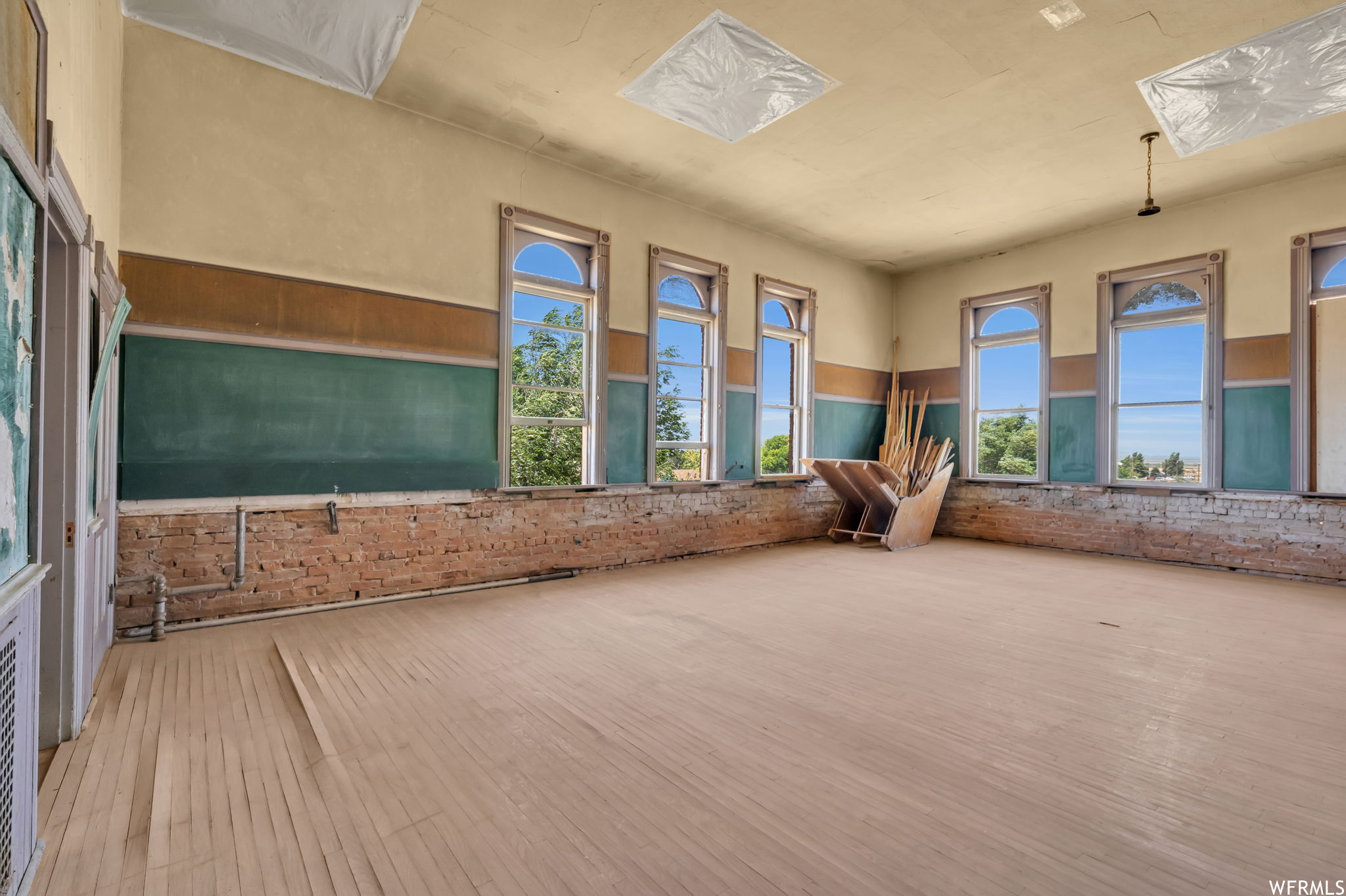 Hardwood floored classroom featuring a healthy amount of sunlight and exposed brick wall
