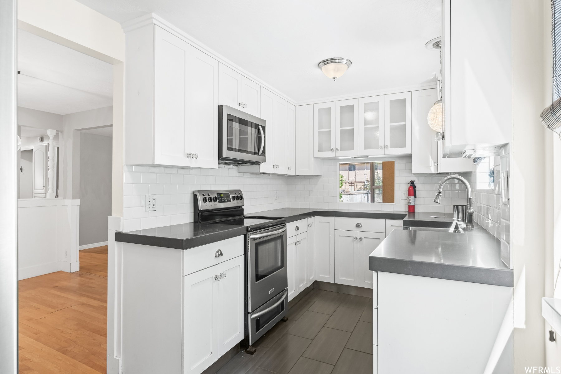 Kitchen with appliances with stainless steel finishes, light parquet floors, white cabinets, and backsplash