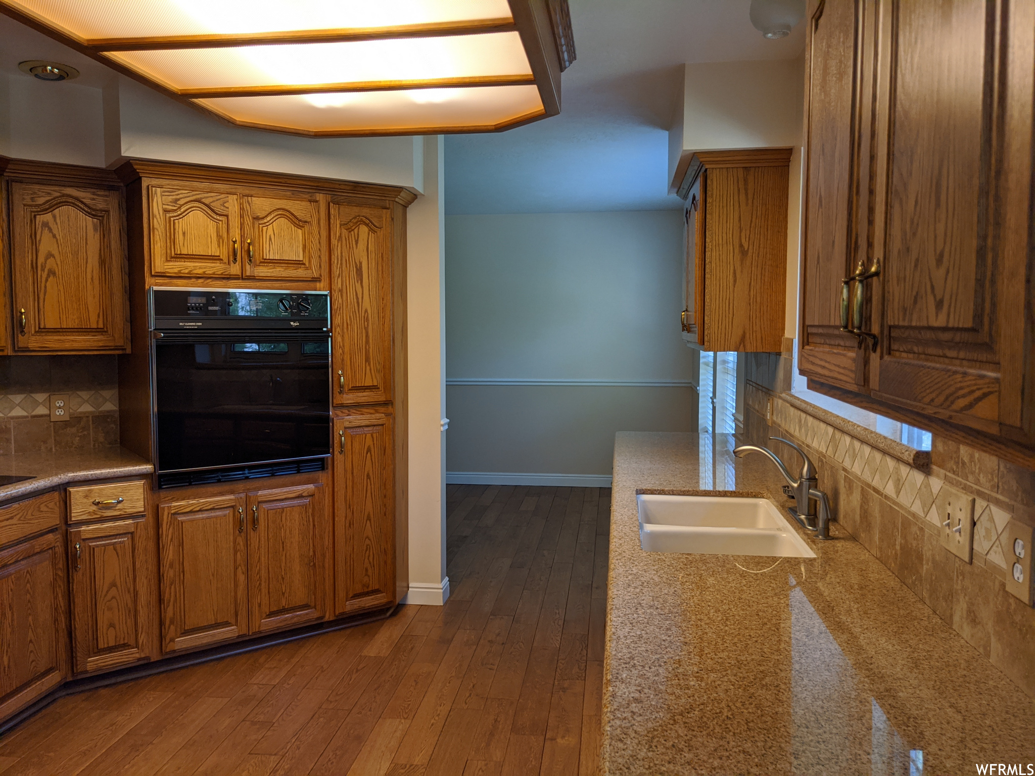 Kitchen with backsplash, brown cabinets, light hardwood floors, and black oven