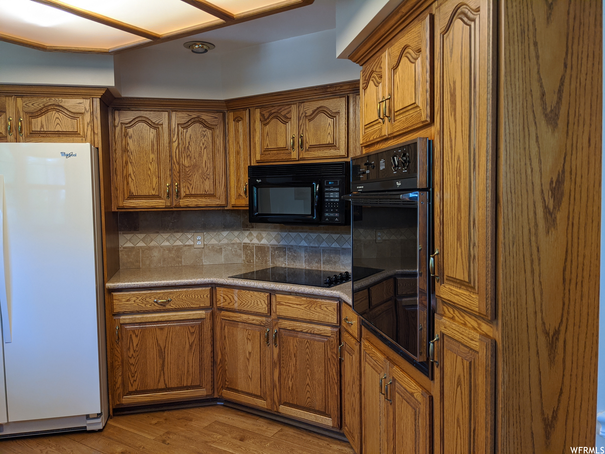 Kitchen featuring brown cabinets, light hardwood floors, backsplash, and black appliances
