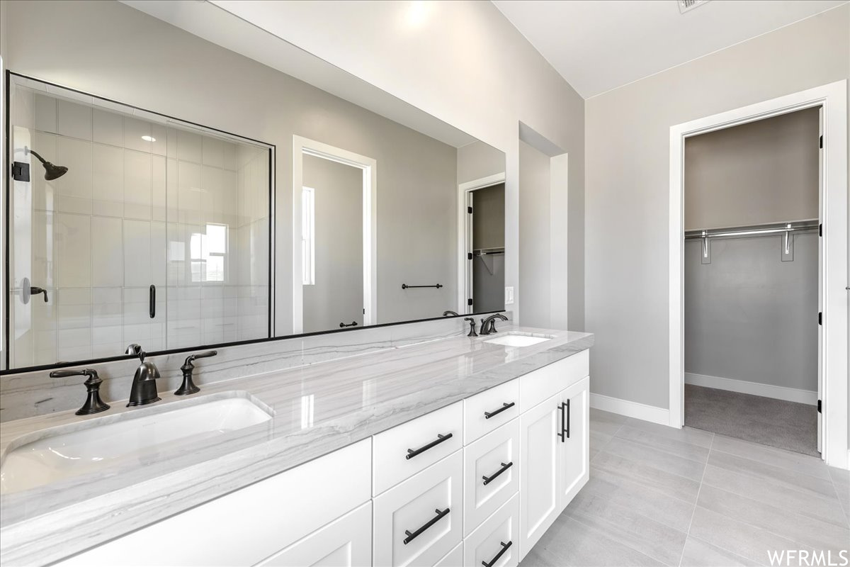 Bathroom featuring tile floors, dual sinks, a shower with shower door, and oversized vanity