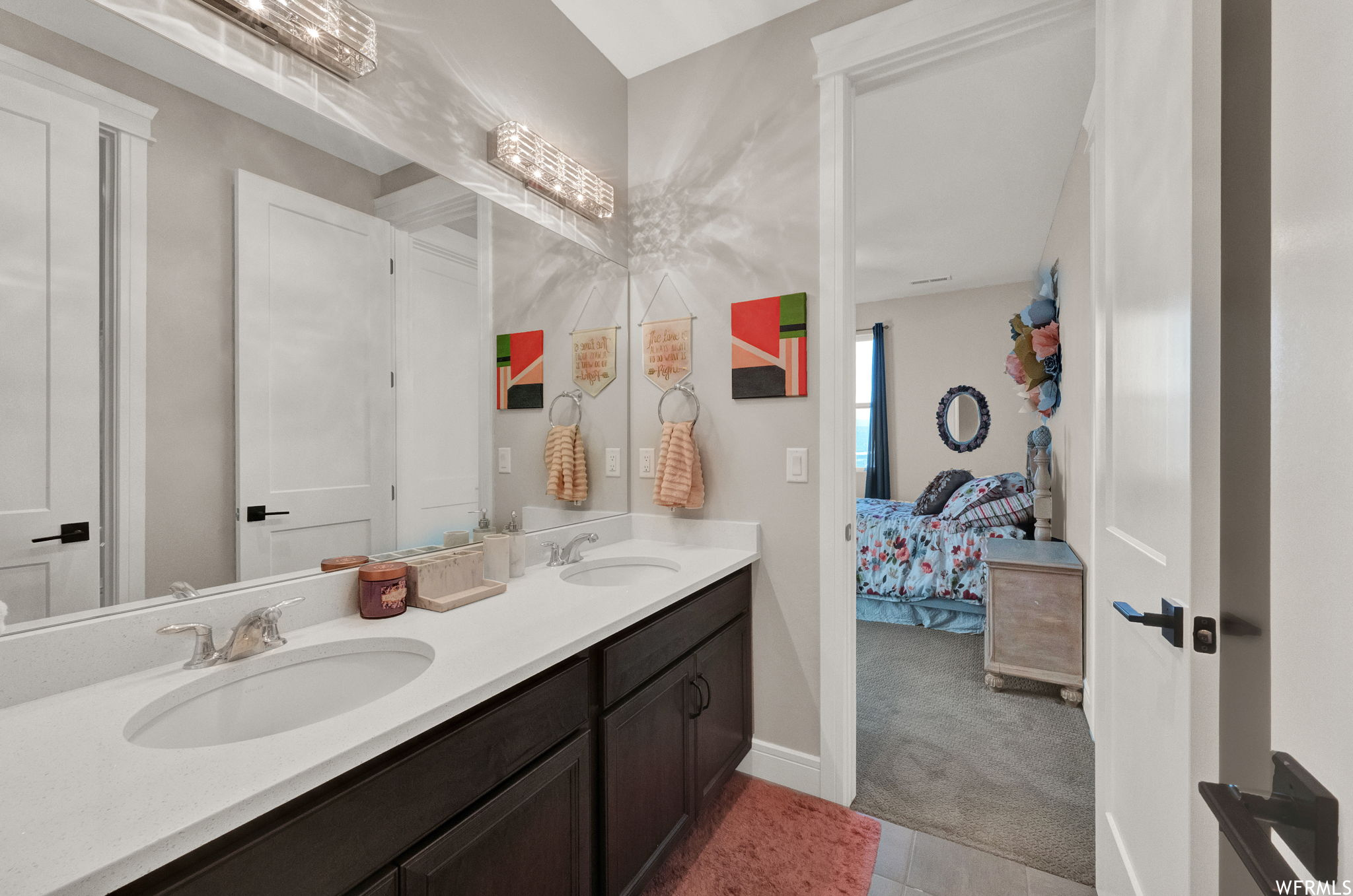Bathroom with double sink vanity, light tile floors, and mirror
